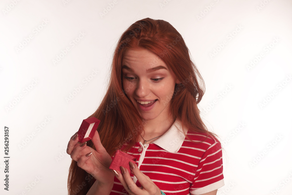The portrait of an young redhead lady with a gift box in her hands isolated over white background posing The portrait of an young redhead lady with a gift box in her hands isolated over white background posing