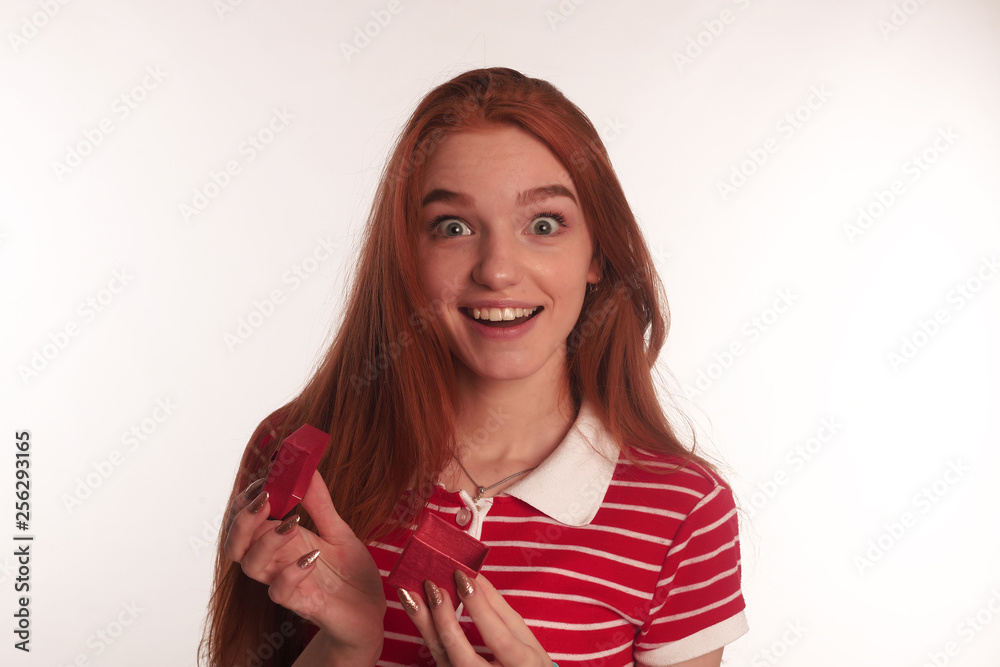 The portrait of an young redhead lady with a gift box in her hands isolated over white background posing