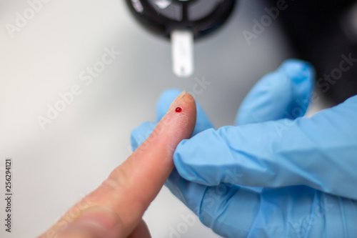 Diabetes patient measuring glucose level blood test using ultra mini glucometer and small drop of blood from finger and test strips isolated on a white background