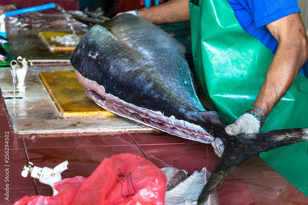 A male worker at the fish market in Male, Maldives, cutting a big tuna fish