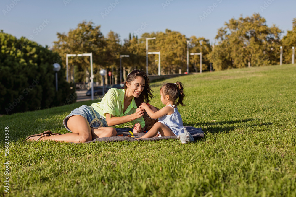 Happy mother playing with daughter on a blanket in park Happy mother playing with daughter on a blanket in park