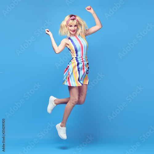 Young fashionable girl Smiling jump in Studio. Beautiful easy-going blonde woman in Stylish summer dress having fun, makeup, Trendy sneakers. Cheerful happy model, funny fashion concept