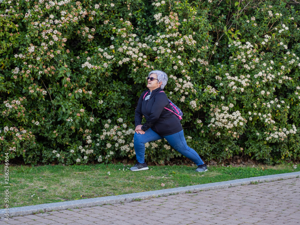 Fototapeta premium A senior woman with white hair practicing gymnastics in an urban park