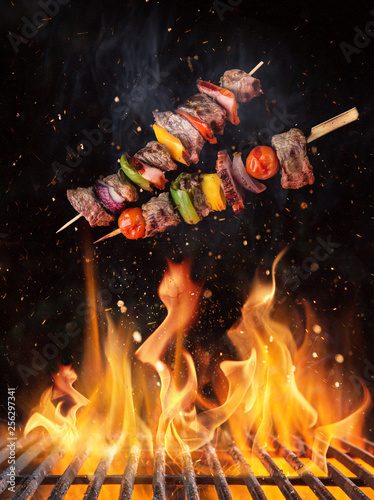 Canvas Print Tasty skewers flying above cast iron grate with fire flames