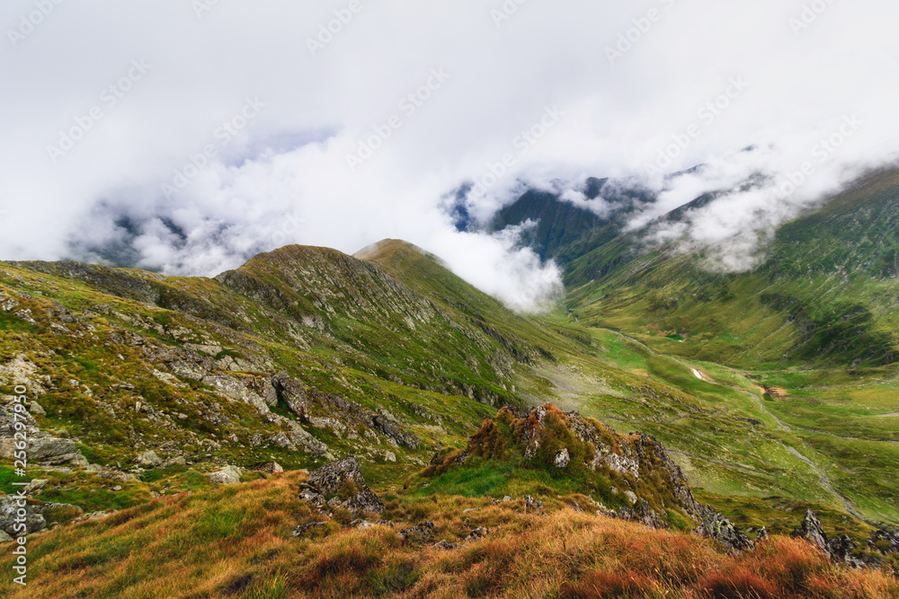 Amazing landscape of summer mountains. View of fog and low clouds over Fagaras Mountains are the highest mountains of the Southern Carpathians. Transylvania. Romania. Travel background. Amazing landscape of summer mountains. View of fog and low clouds over Fagaras Mountains are the highest mountains of the Southern Carpathians. Transylvania. Romania. Travel background.