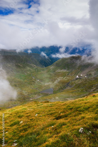 Amazing landscape of summer mountains. View of fog and low clouds over Fagaras Mountains are the highest mountains of the Southern Carpathians. Transylvania. Romania. Travel background. 