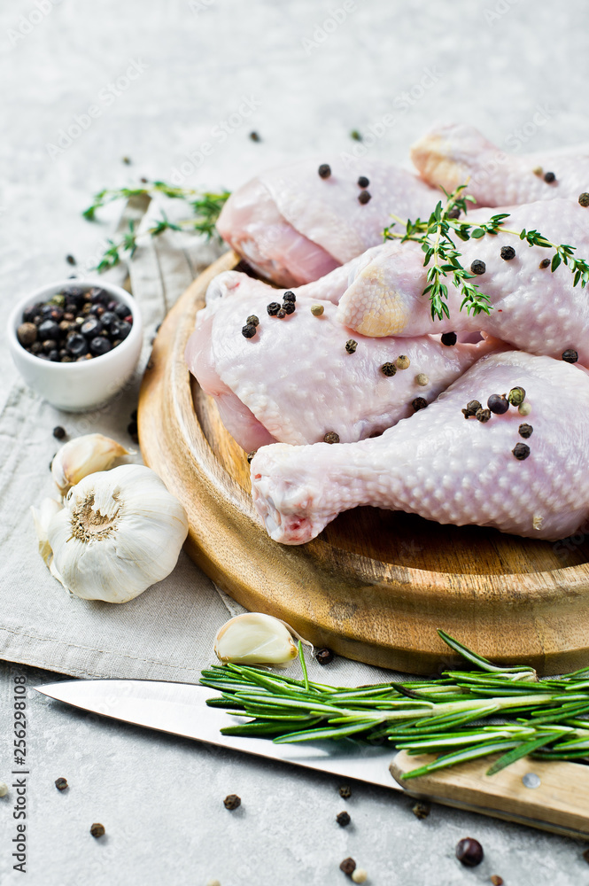 Raw chicken legs. Ingredients for cooking: rosemary, thyme, garlic, pepper. Gray background, side view.