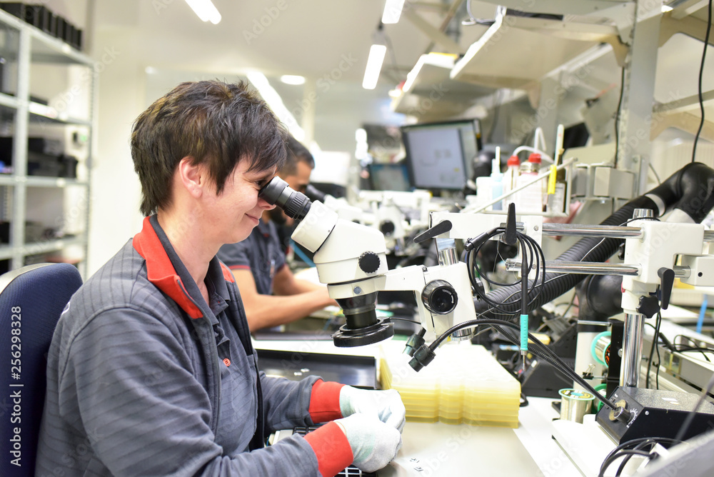 Woman using a microscope for the quality control in the manufacturing of circuit boards for the electronics industry Woman using a microscope for the quality control in the manufacturing of circuit boards for the electronics industry