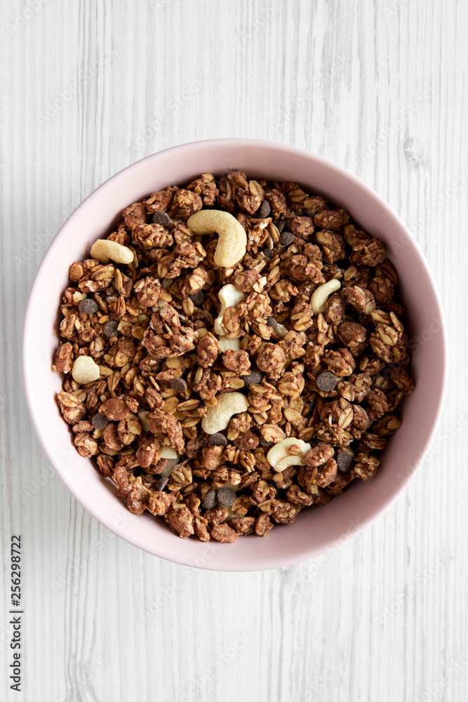 Homemade chocolate granola with nuts in a pink bowl over white wooden background, top view. From above, overhead. Homemade chocolate granola with nuts in a pink bowl over white wooden background, top view. From above, overhead.
