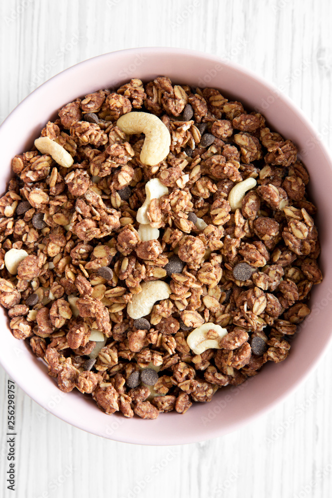 Homemade chocolate granola with nuts in a pink bowl over white wooden surface, top view. From above, overhead. Close-up. Homemade chocolate granola with nuts in a pink bowl over white wooden surface, top view. From above, overhead. Close-up.