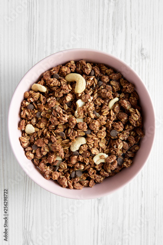 Homemade chocolate granola with nuts in a pink bowl over white wooden background, top view. From above, overhead.