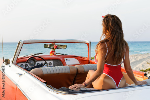Sexy woman wearing red swimsuit is sitting inside a retro cabriolet car