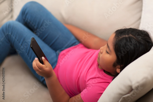 Elementary age student sitting on a couch while at home and using a mobile phone.