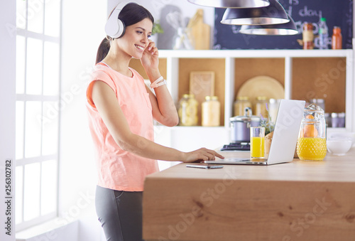Young woman in kitchen with laptop computer looking recipes, smiling. Food blogger concept.