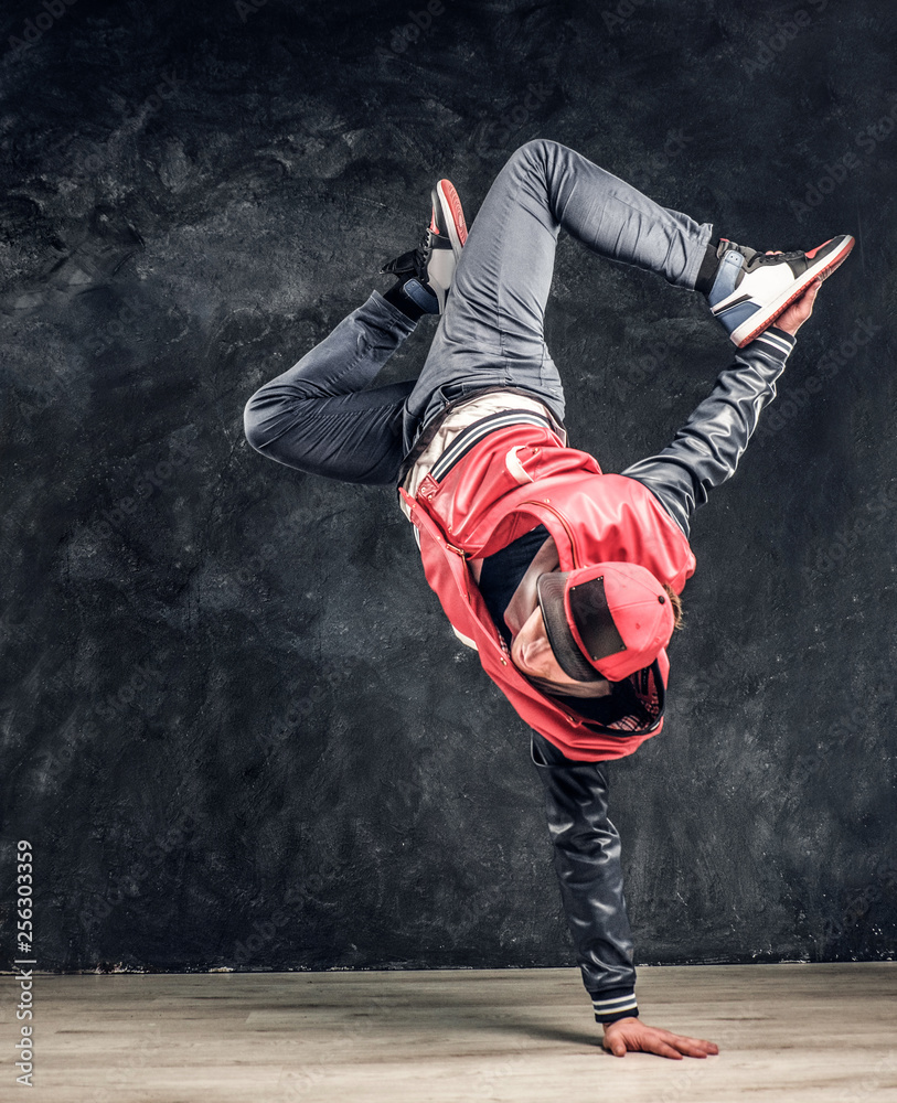 Stylish guy performs breakdance acrobatic elements. Studio photo against a dark textured wall