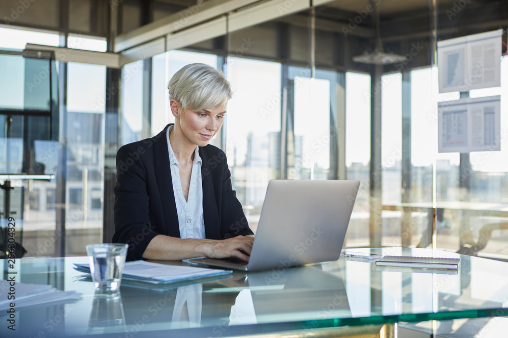 Businesswoman sitting at desk in office using laptop Businesswoman sitting at desk in office using laptop