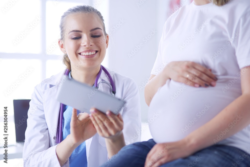 Smiling woman doctor shows pictures on the tablet to pregnant young woman at hospital. Smiling woman doctor shows pictures on the tablet to pregnant young woman at hospital.