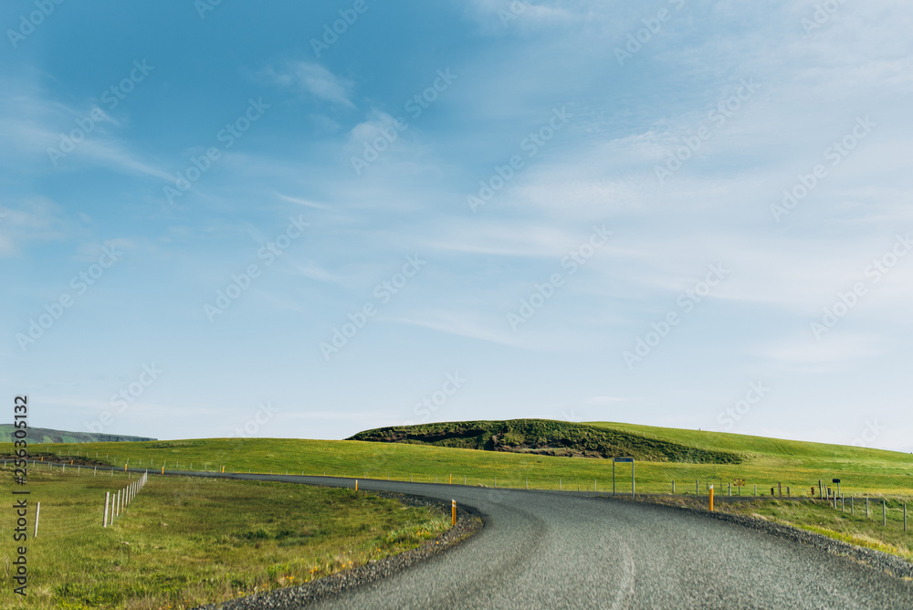 Asphalt road between green grass. The road is on the background of a blue sky. Asphalt road in Iceland.