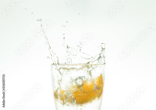 Slice the orange slice in a glass of water and make a spray on a white background. water spray in the air. a slice of citrus drops in a glass spray.