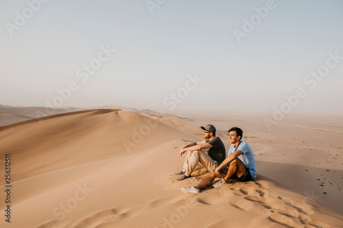 Namibia, Namib, two friends sitting on desert dune looking at view photo