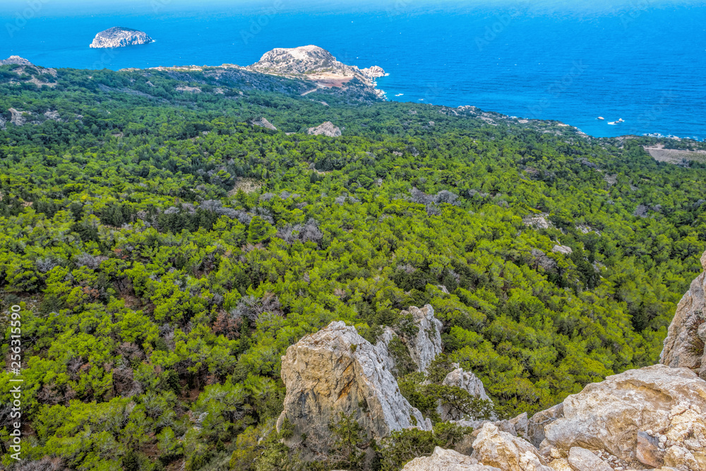 Panoramic view of the coastal rocks of the Mediterranean Sea, overgrown with green forest in the early summer morning. Rhodes island, Greece. Panoramic view of the coastal rocks of the Mediterranean Sea, overgrown with green forest in the early summer morning. Rhodes island, Greece.