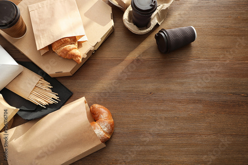 Paper bags with pastry and takeaway food on wooden table, top view. Space for text