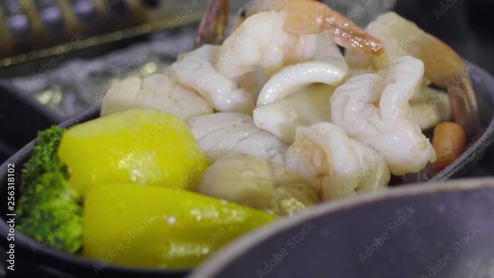 hands placing various steamed vegetables and seafood on plate with chopsticks close up. hands placing various steamed vegetables and seafood on plate with chopsticks close up.