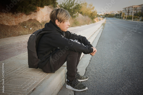 Blond teenager in black clothe sitting on street border  photo