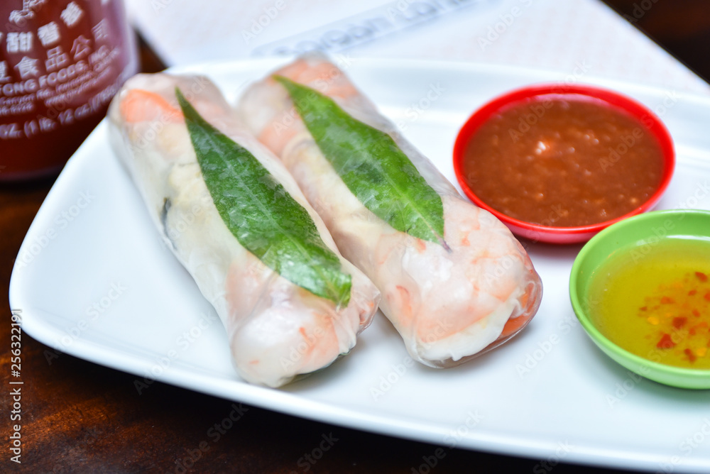 Traditional Vietnamese cuisine dish - fresh spring rolls wrapped in transparent rice paper with prawns, vermicelli, mint and carrots inside served with spicy sauces