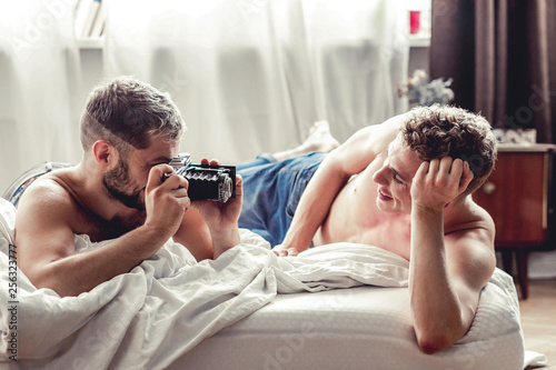 Gay man taking picture of his partner with old-fashioned camera in bed