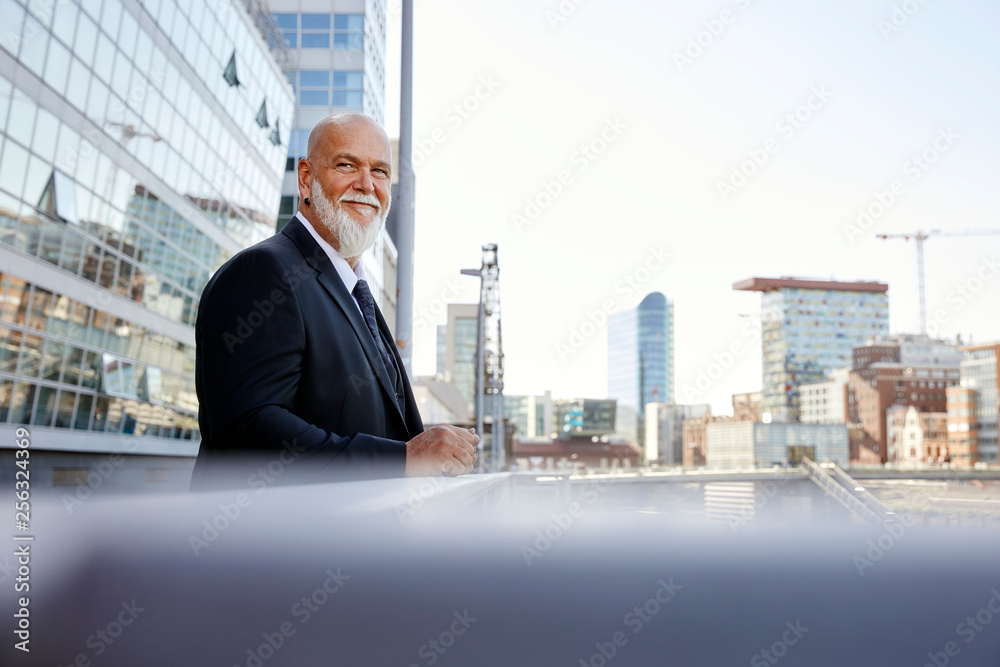 Elegant businessman leaning on railing in the city, smiling Elegant businessman leaning on railing in the city, smiling