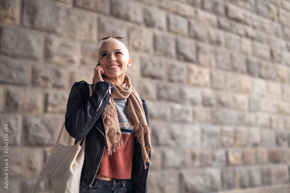Young modern bald woman talking on her cell phone, enjoying a beautiful day outside in an urban city area Young modern bald woman talking on her cell phone, enjoying a beautiful day outside in an urban city area