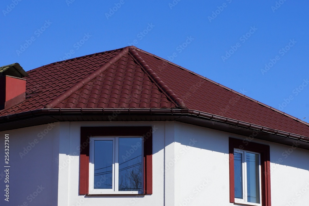 red tile on the roof of the attic of a large private building with a window against the blue sky on the street