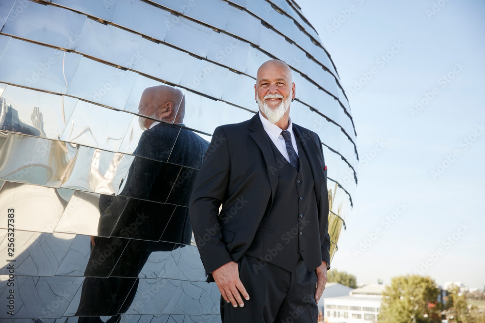 Elegant businessman smiling in the city, laughing in front of mirror facade Elegant businessman smiling in the city, laughing in front of mirror facade