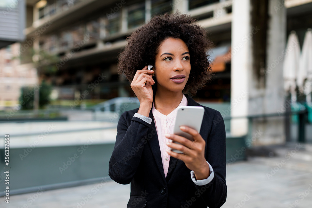 Portrait of businesswoman with smartphone putting on earphones Portrait of businesswoman with smartphone putting on earphones