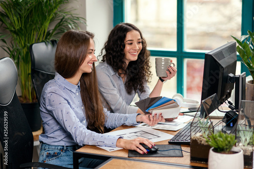 Two beautiful female designers or architects jointly solve work tasks while working in modern office near window. Creative people or advertising business concept.