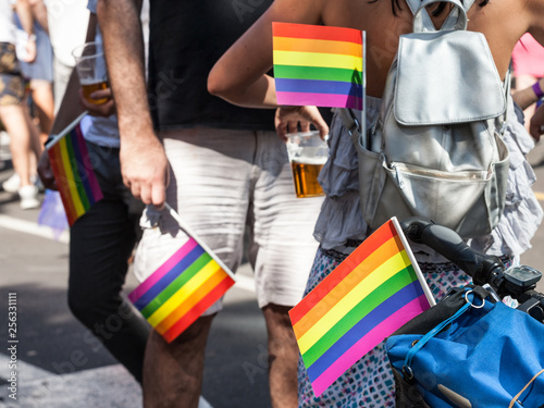 Two men and a woman holding rainbow gay flags in their pockets during a Gay Pride. The rainbow flag is one of the symbols of the LGBTQ community