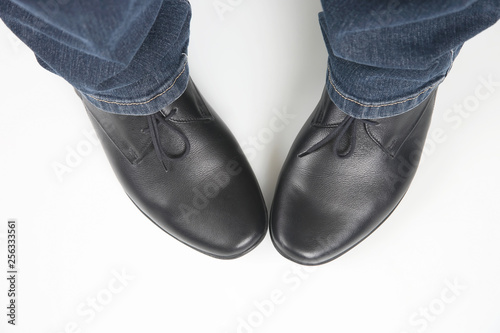 Men's legs in jeans and black classic shoes on white background
