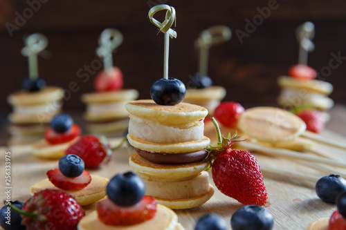 Fruit, berry and pancake canapes on wooden table