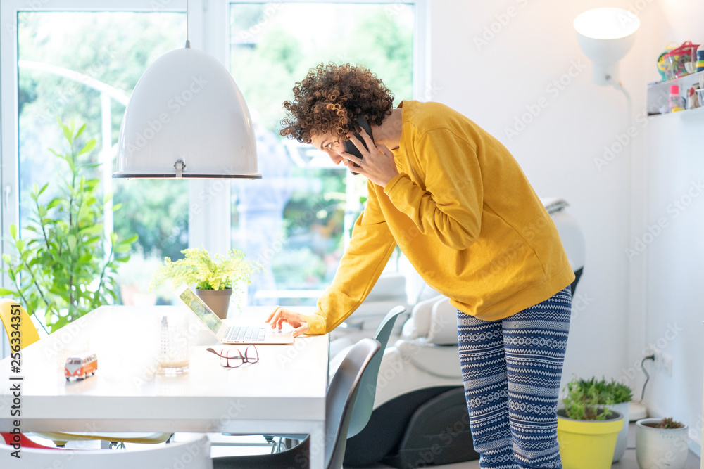 Woman using laptop and cell phone on table at home Woman using laptop and cell phone on table at home