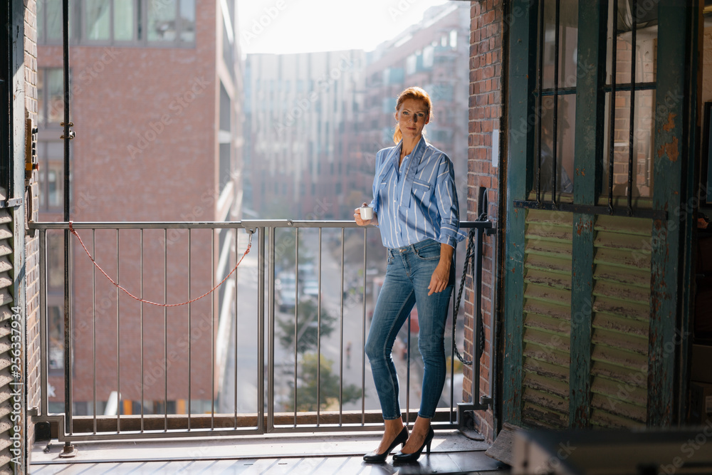Germany, Hamburg, Speicherstadt, businesswoman with cup of coffee standing at the window with view over the city