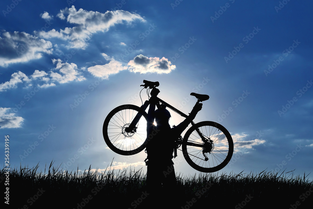 silhouette of a cyclist with a raised bike in the grass in the sun.