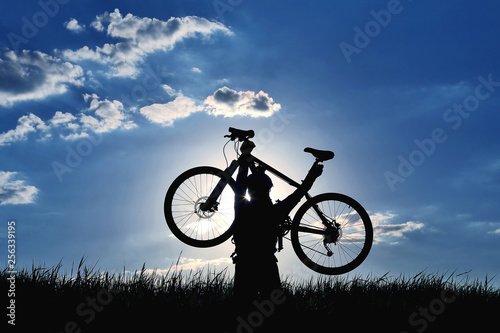 silhouette of a cyclist with a raised bike in the grass in the sun.