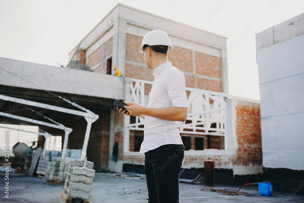 Young caucasian master with a tablet in his hands looking at the building in construction. Young caucasian master with a tablet in his hands looking at the building in construction.
