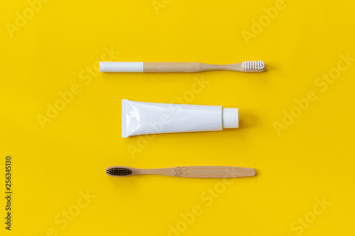 Two natural eco-friendly bamboo brushes with white and black bristles and tube of toothpaste. Set for washing on yellow paper background. Copy space for text or your design Top view Flat lay.