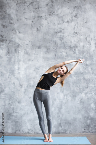 Girl doing yoga exercises on a blue yoga mat full-length in the studio.