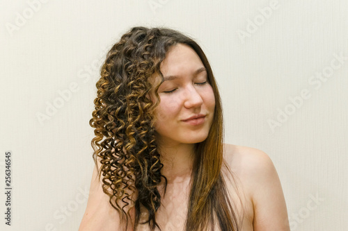 Beautiful young woman with straight and curly hair on a light background. Uncertainty in hair. 