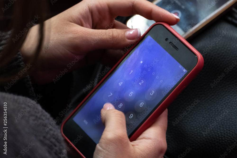 Red mobile phone in female hands. A girl is calling or dialing numbers pin code on a blue screen smartphone similar to an iPhone. Close-up. Red mobile phone in female hands. A girl is calling or dialing numbers pin code on a blue screen smartphone similar to an iPhone. Close-up.