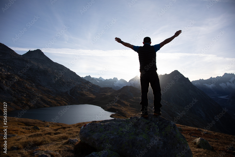 Hiker is standing on a rock with raised hands and enjoying sunrise in the Alps in Switzerland