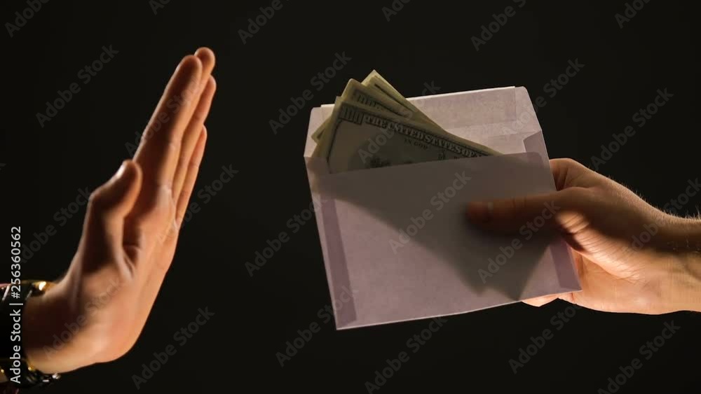 Hand shows stop gesture to envelope with dollars, refusing corrupt money, bribe Hand shows stop gesture to envelope with dollars, refusing corrupt money, bribe